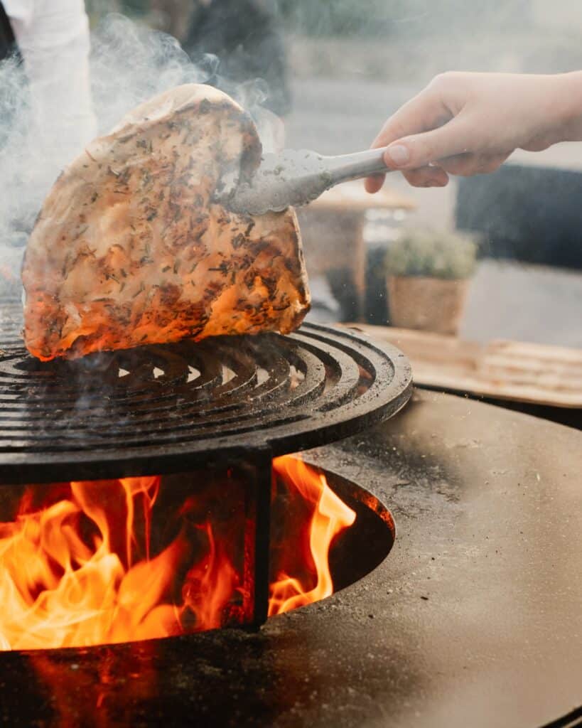 Cuisson de pain plat au barbecue : saveurs au feu de bois Pain plat artisanal aux herbes saisi sur un gril circulaire au-dessus de flammes vives en plein air.
