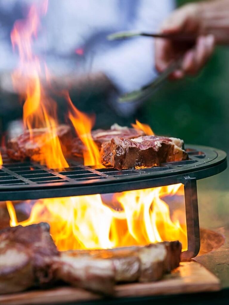 Grillade de steaks sur brasero : Maîtrise de la flamme Steaks épais grillant sur un brasero avec des flammes vives lors d'un barbecue en plein air convivial.