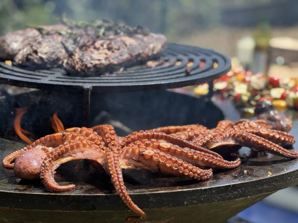 Barbecue de Poulpe et Viande : Cuisson au Brasero Plancha Poulpe grillé et viande sur un brasero plancha en plein air avec flammes vives pour un barbecue convivial.