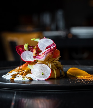 Salade gastronomique avec radis croquants, endives rouges et graines sur une assiette noire élégante.