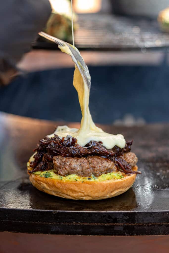 Burger Gourmet au Fromage Fondu et Oignons Caramélisés Fromage fondu étiré sur un burger gourmet au bœuf grillé et oignons caramélisés, préparation appétissante.